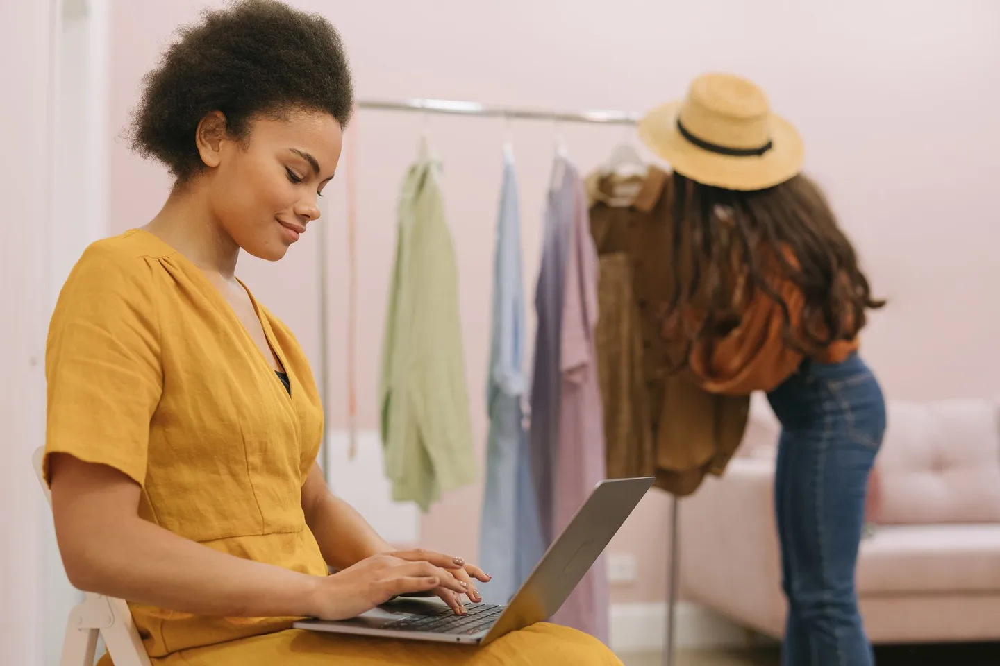 Mulher de vestido amarelo trabalhando em um notebook em uma pequena loja de roupas